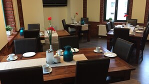 A dining area with wooden tables and chairs, a flat-screen TV mounted on the wall, and a brick wall. - Pension Alabama (Lutherstadt Wittenberg)