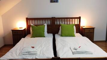 A double bed with white linens and green pillows, flanked by wooden nightstands with lamps, in a room with a sloped ceiling and a painting above the bed.