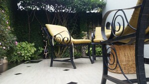 A patio area with outdoor furniture, including a chair and a table, surrounded by lush greenery and a tiled floor. - Raha Leo Inn (Arusha)