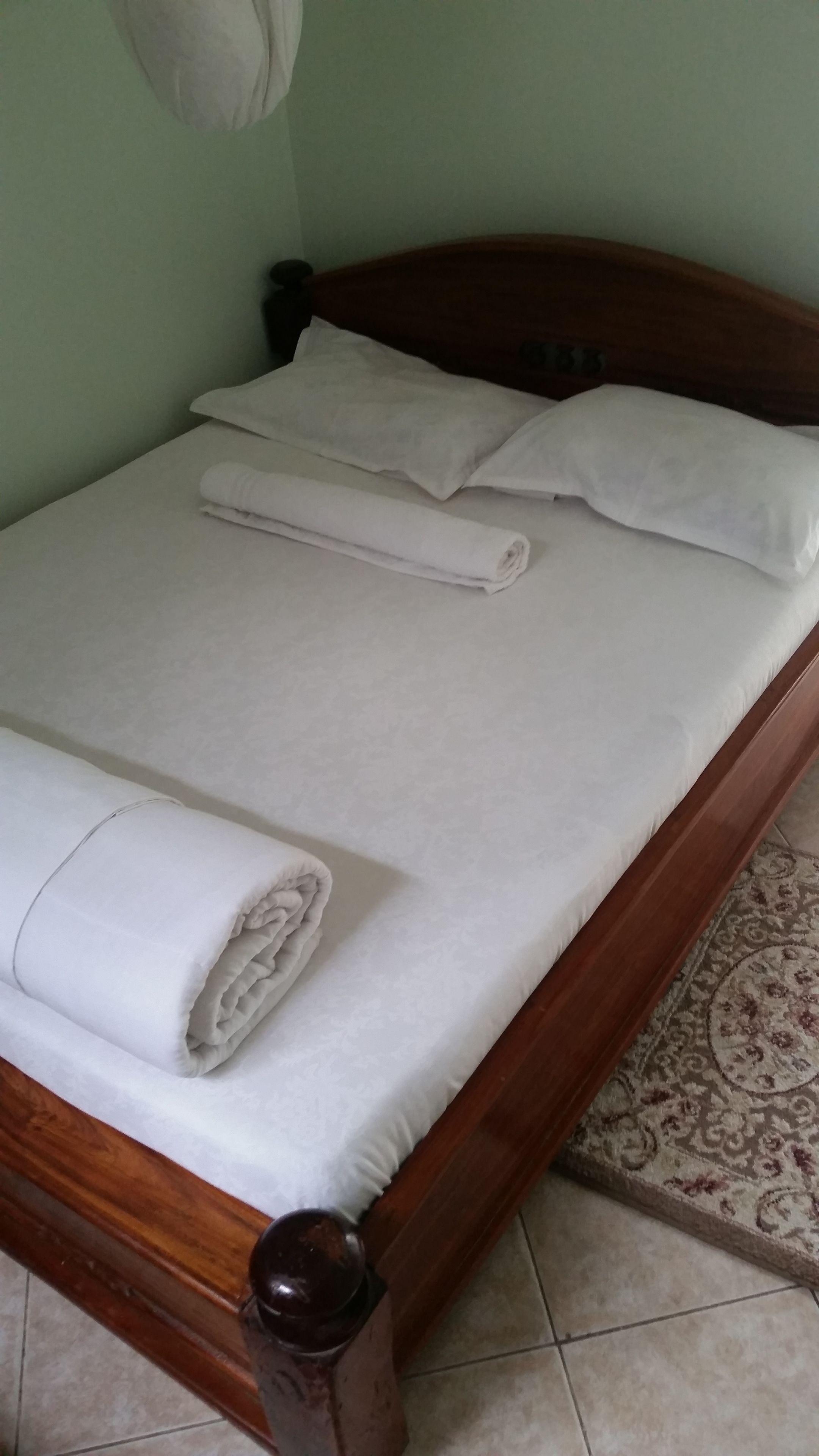 A neatly made bed with white linens and pillows, a wooden headboard, and a patterned rug on the floor.