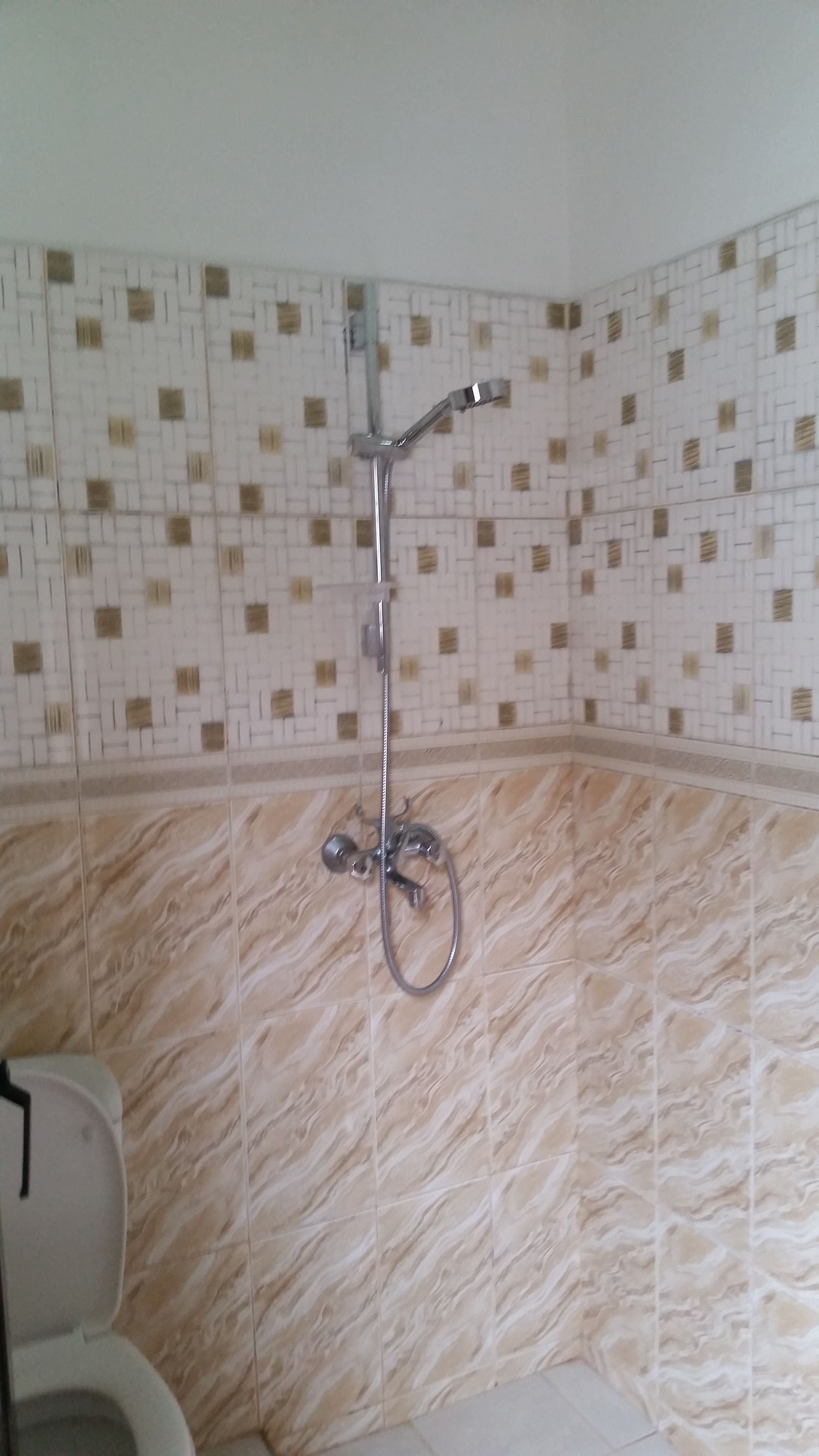 Ein Badezimmer mit Dusche, geflieste Wände und einem marmorähnlichen Boden.