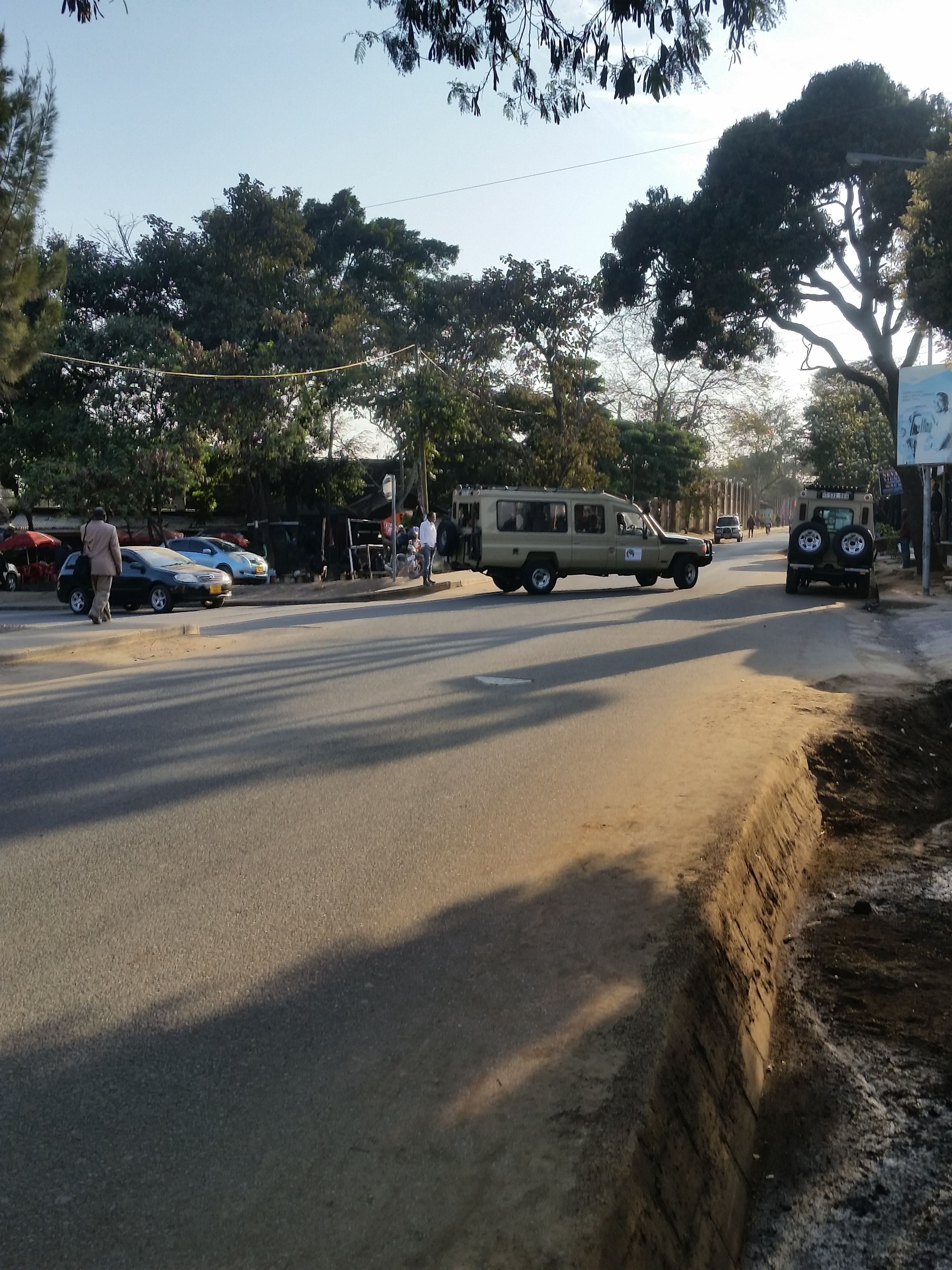Escena callejera con un sendero de tierra junto a la carretera, vehículos y árboles.