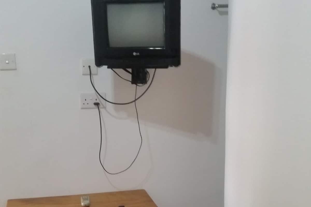 A small room with a wooden table and a chair, a wall-mounted television, and a door.