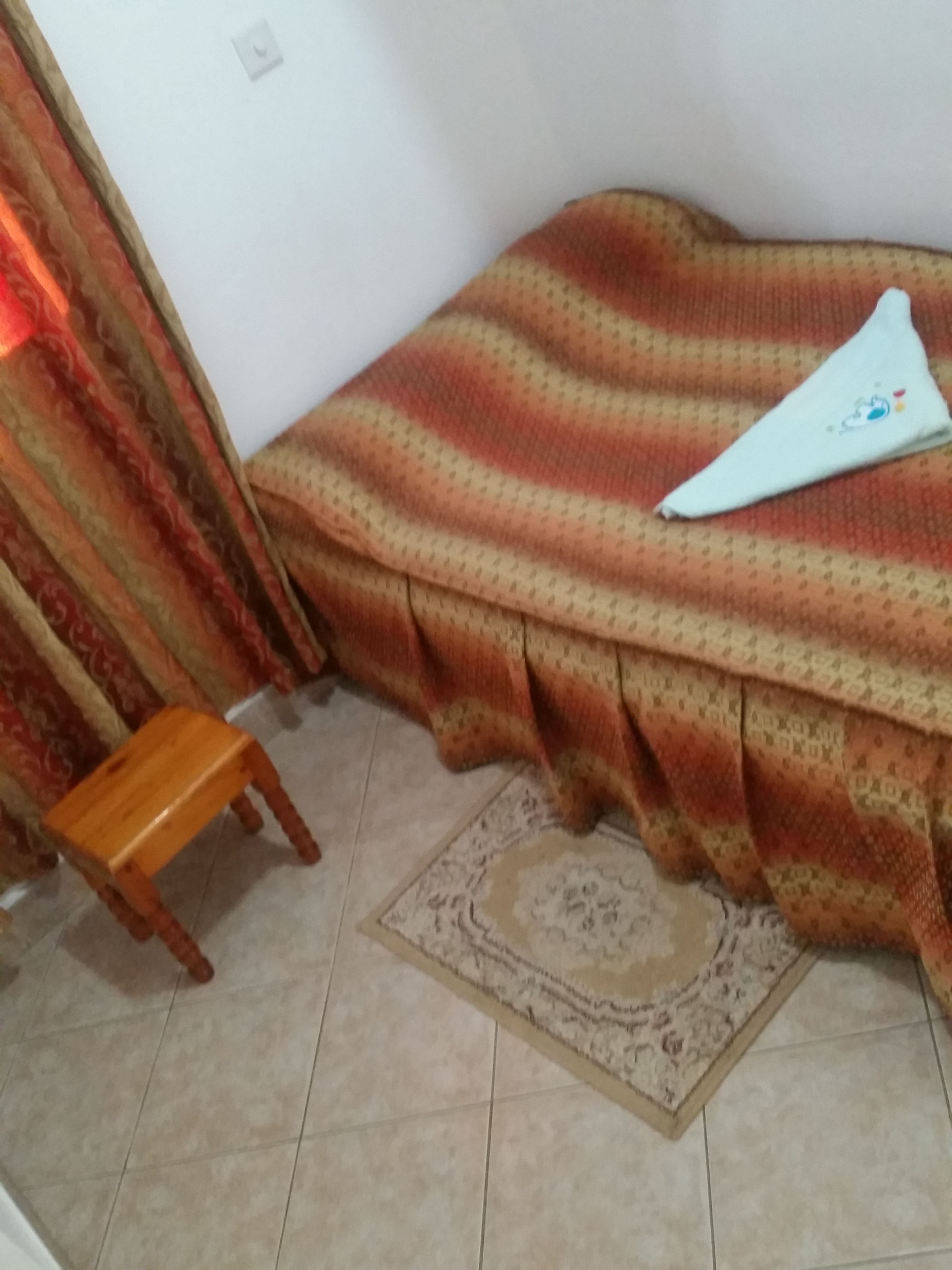Una habitación con una cama cubierta por un edredón estampado, un taburete de madera y una alfombra decorativa.