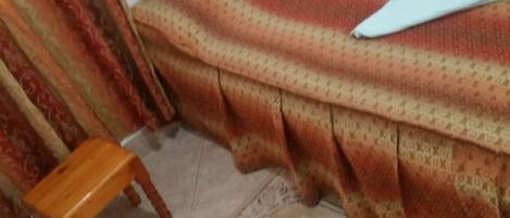 Una habitación con una cama cubierta por un edredón estampado, un taburete de madera y una alfombra decorativa.