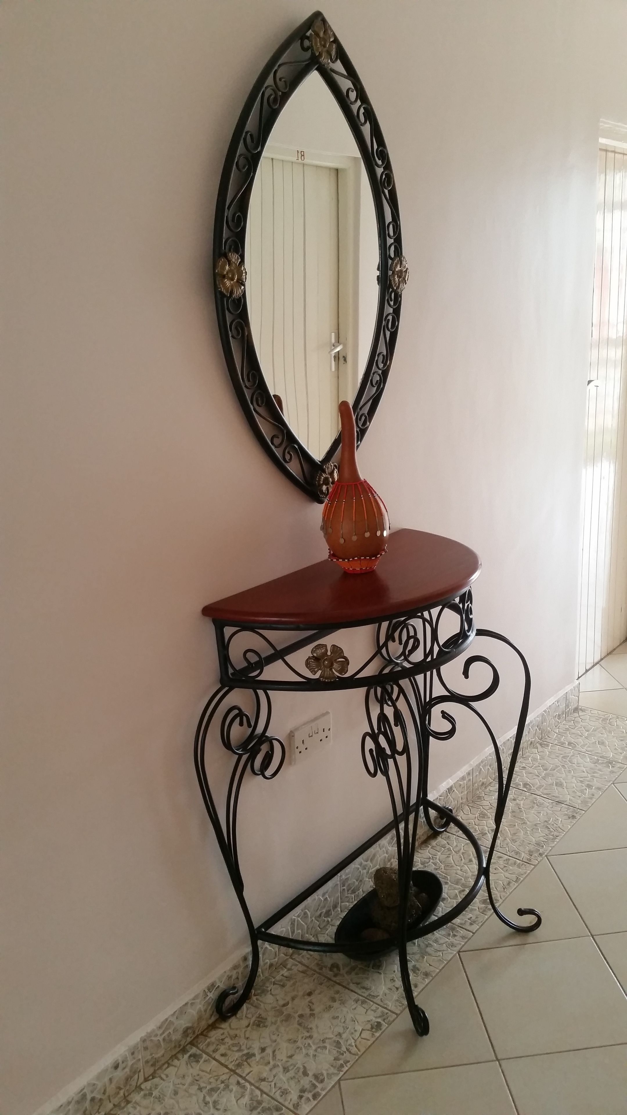 A corner with a decorative mirror, a small table with a vase, and a tiled floor.