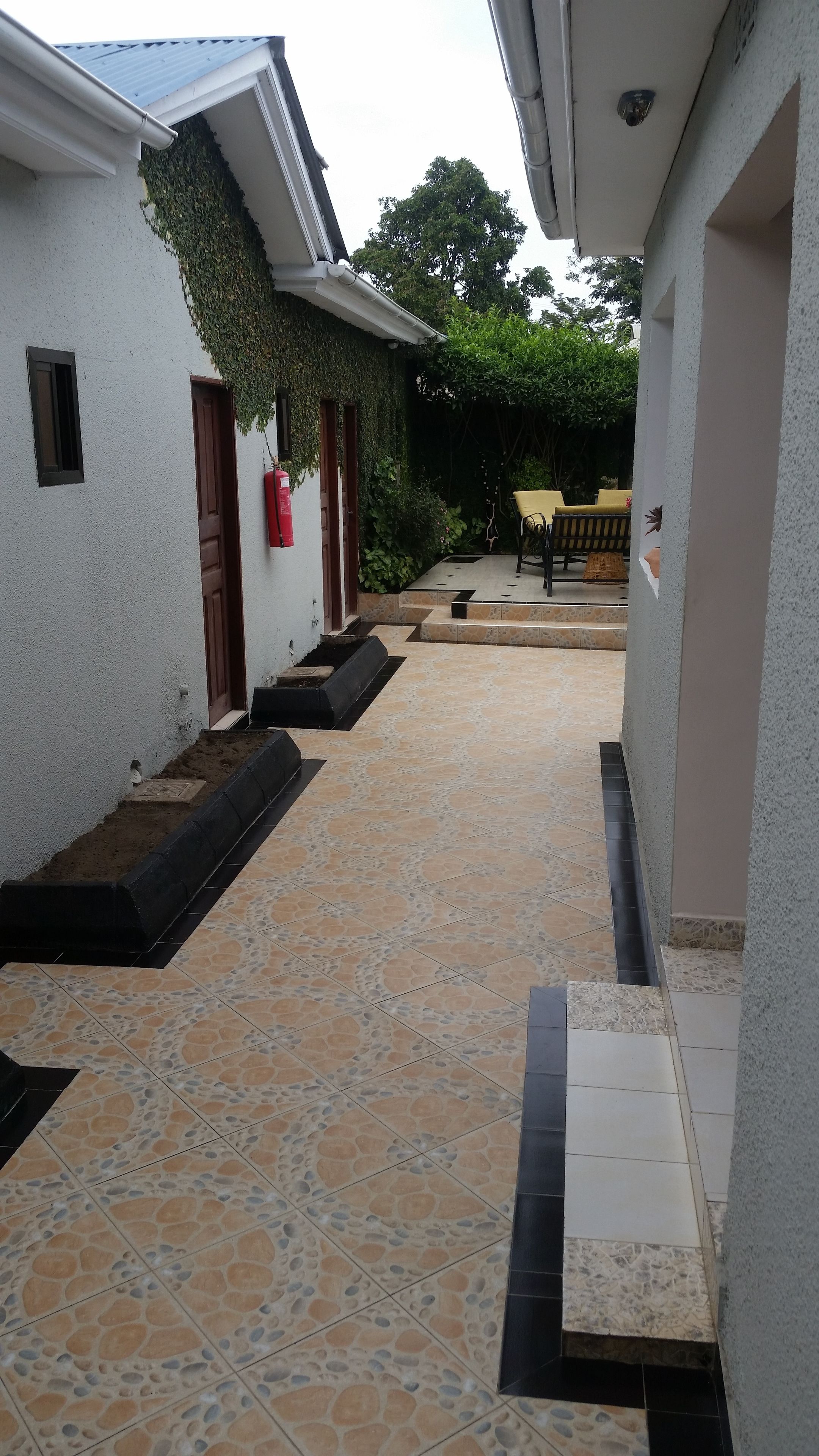 A covered outdoor area with tiled flooring, a fire extinguisher, and a bench.