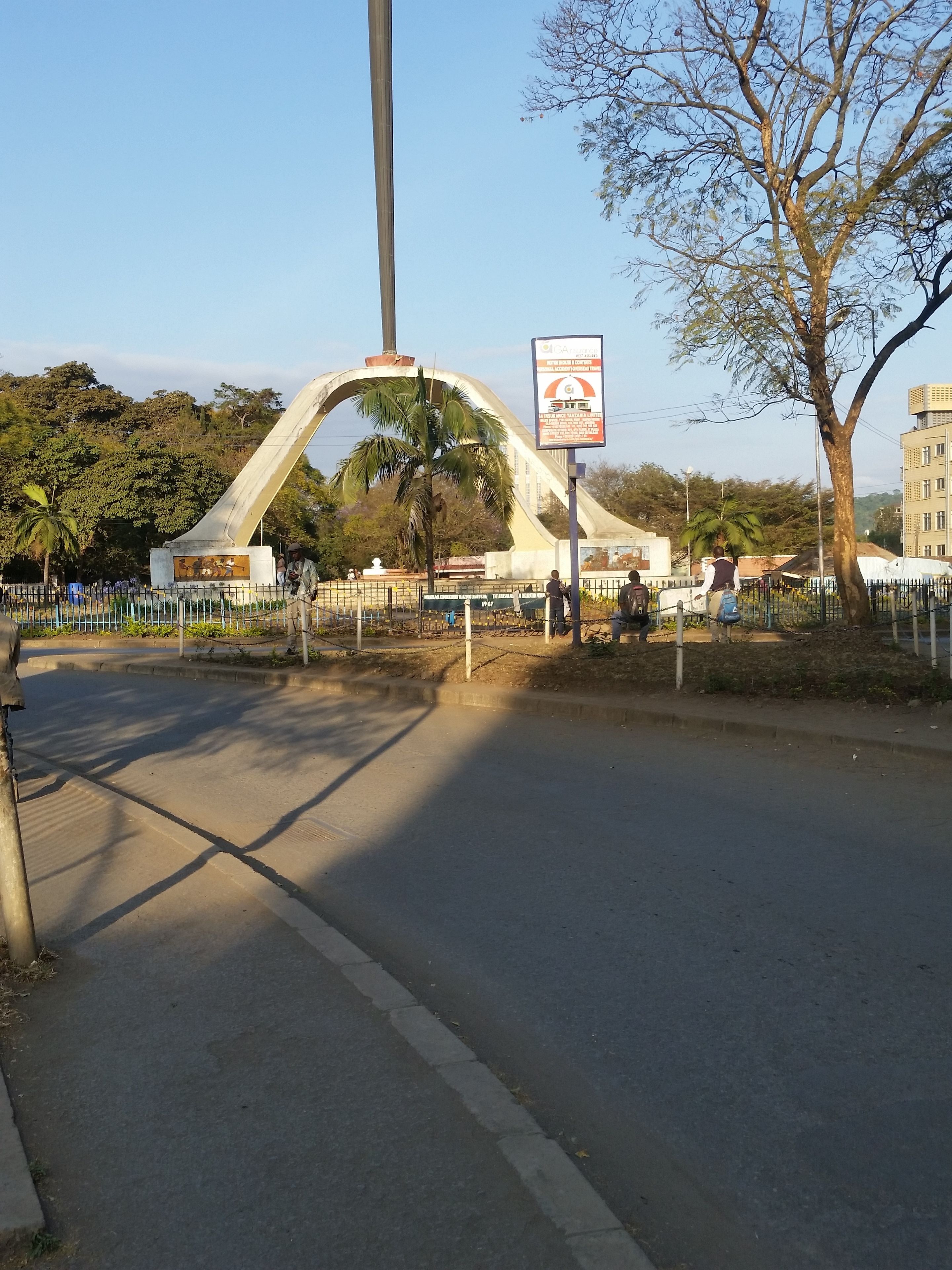 Una intersección de caminos con un gran monumento en arco, una señal y un área cercada con árboles.