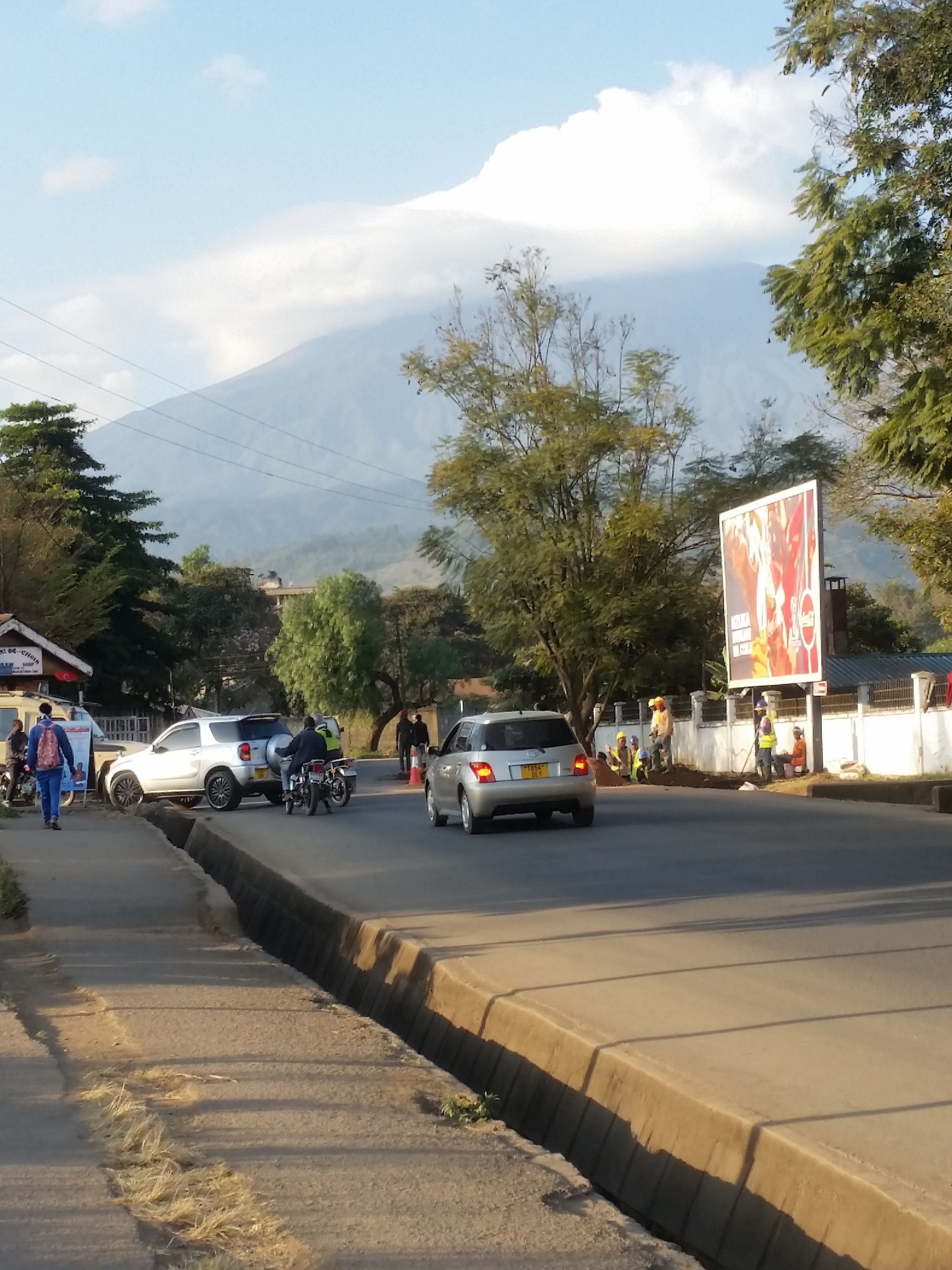 A street scene with a mountain in the background, vehicles, and pedestrians.