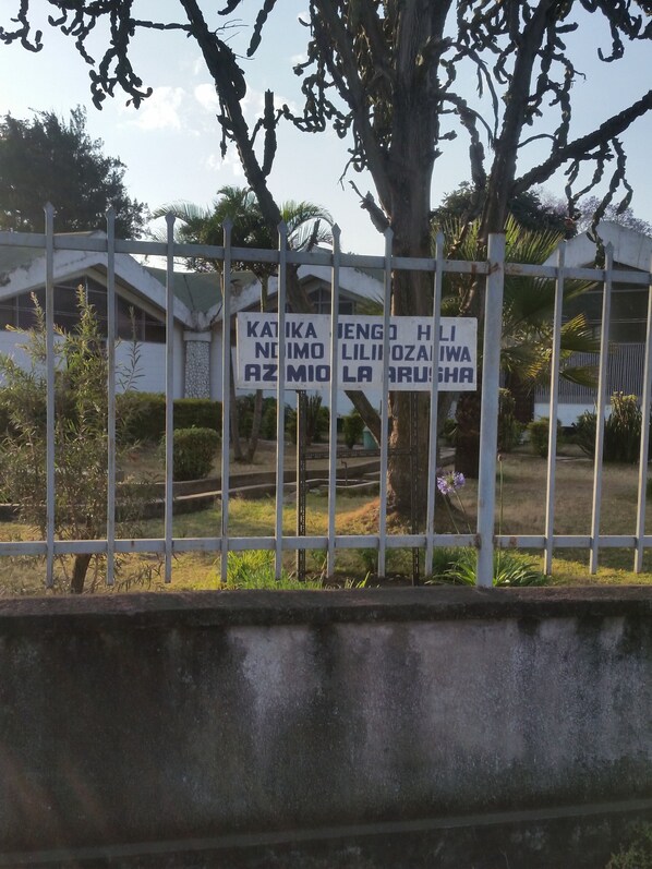 A gated area with a sign in a foreign language, a tree, and a building in the background.