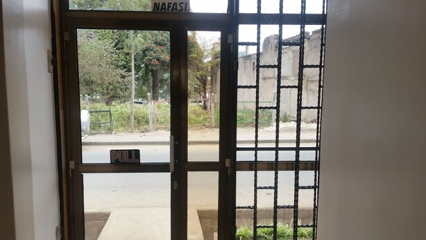 A gated entrance with a 'PULL' sign, a metal gate, and a view of a road and greenery outside. - Raha Leo Inn (Arusha)