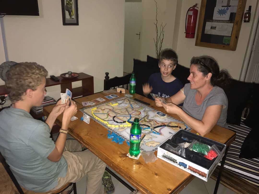 Een groep mensen speelt een spel aan een houten tafel, met een kaart, kaarten en speelstukken.