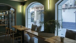 A cozy cafe with wooden tables and chairs, large windows with arched tops, and a potted plant on one table. - Alda Jolio Jaca (Jaca)
