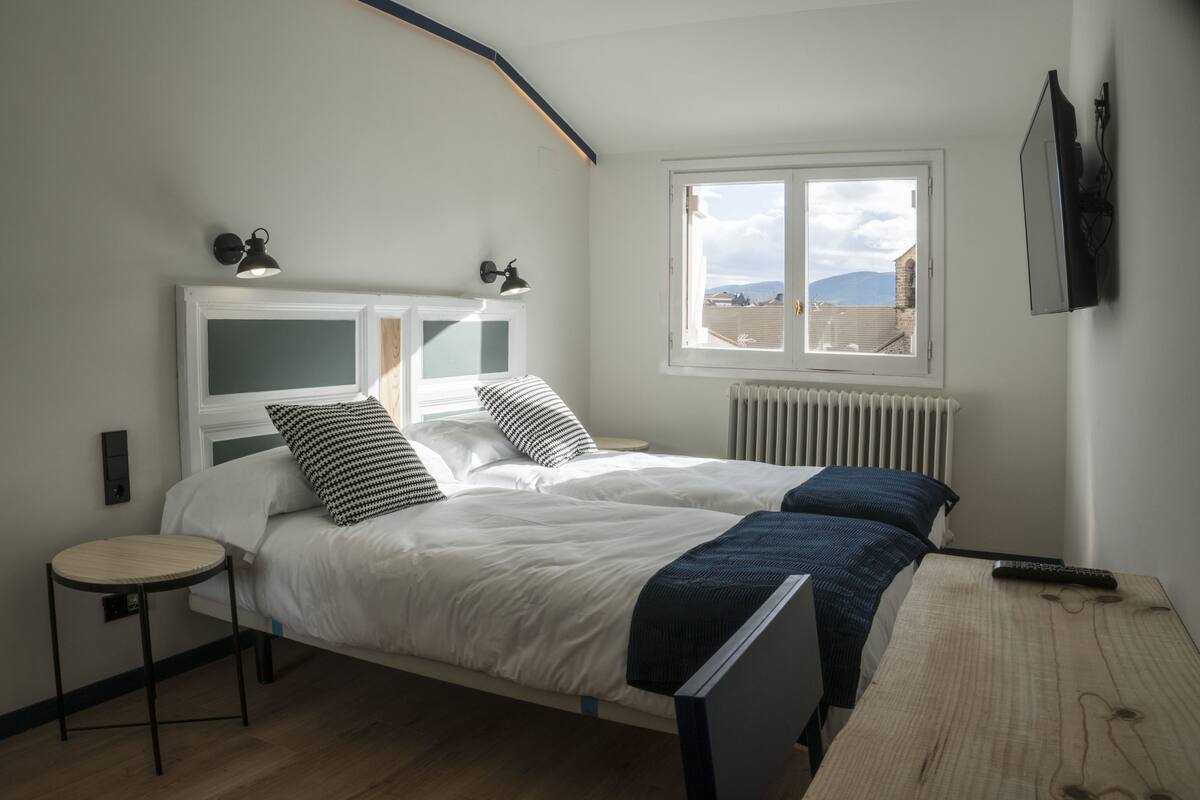 Un dormitorio con cama, mesitas de noche, ventana con vistas y un radiador.