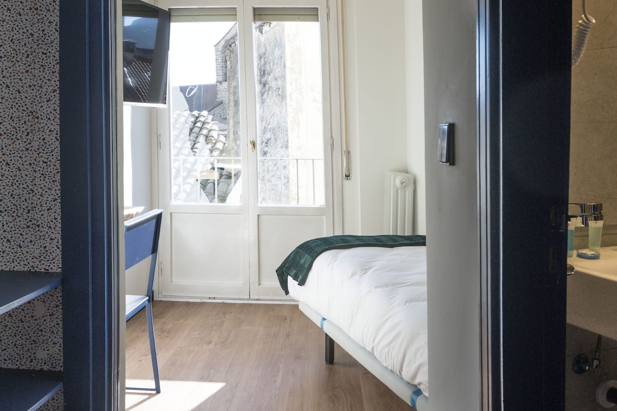 Un dormitorio con cama, una silla, una ventana y una puerta que da a un balcón.