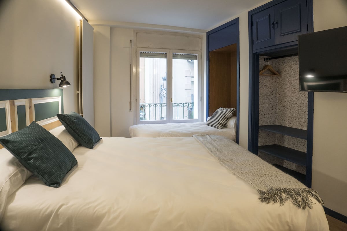 Un dormitorio con dos camas, televisor, armario y balcón con vistas.