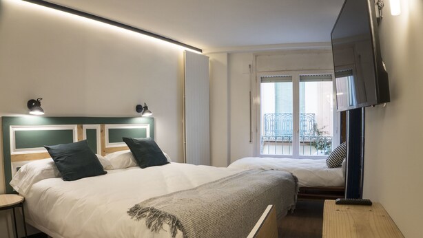 A hotel room with two beds, a TV, a balcony view, and a small table. - Alda Jolio Jaca (Jaca)