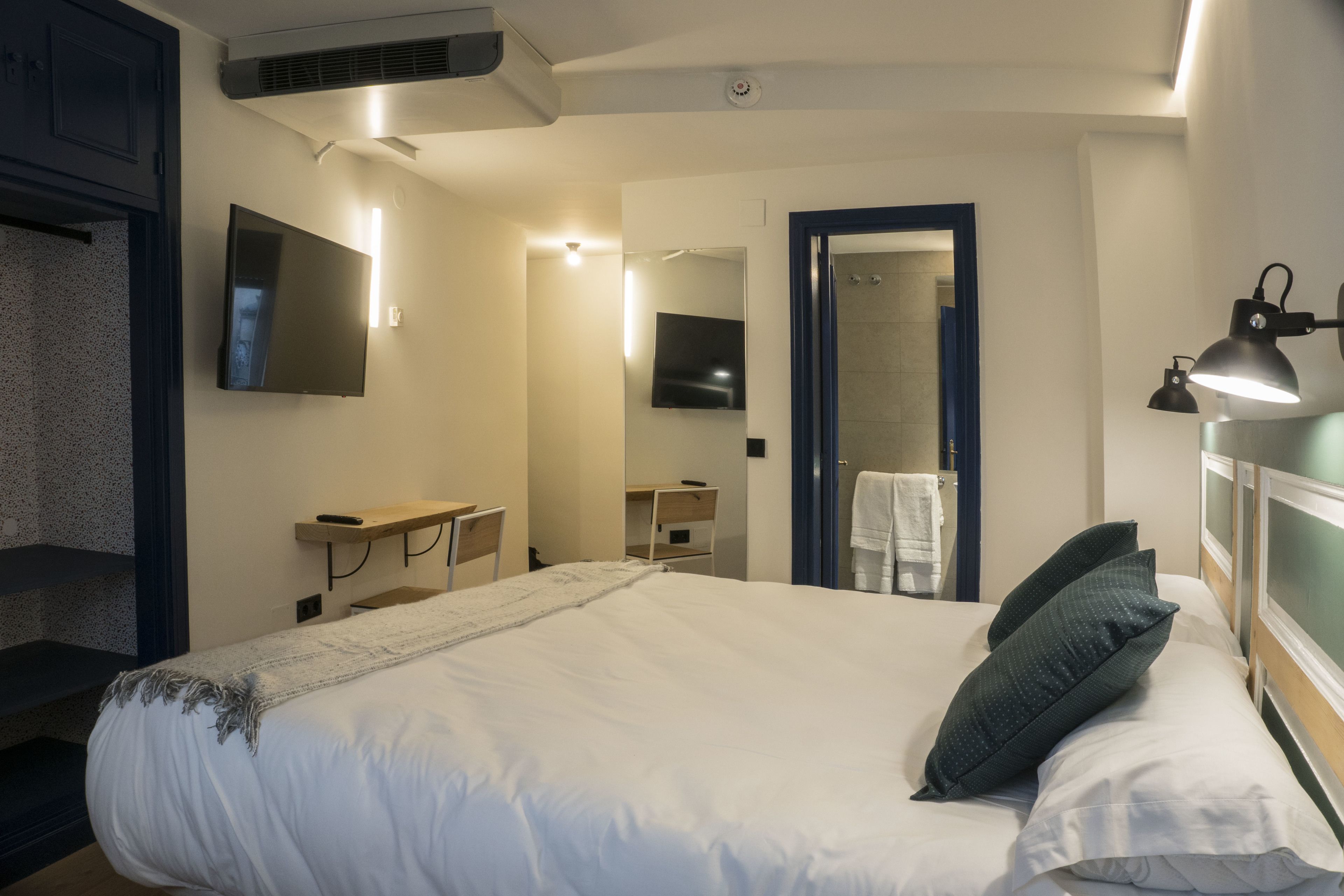 A hotel room with a large bed, a desk, a mirror, a TV, and a shower area.