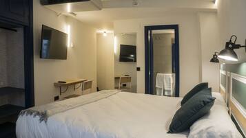 A hotel room with a large bed, a desk, a mirror, a TV, and a shower area.