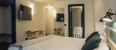 A hotel room with a large bed, a desk, a mirror, a TV, and a shower area.