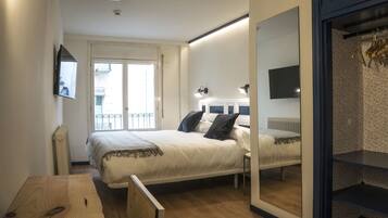 Un dormitorio con cama, mesita de noche, espejo y vistas al balcón exterior.