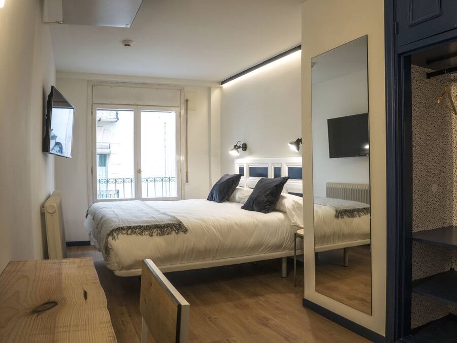 Un dormitorio con cama, mesita de noche, espejo y vistas al balcón exterior.