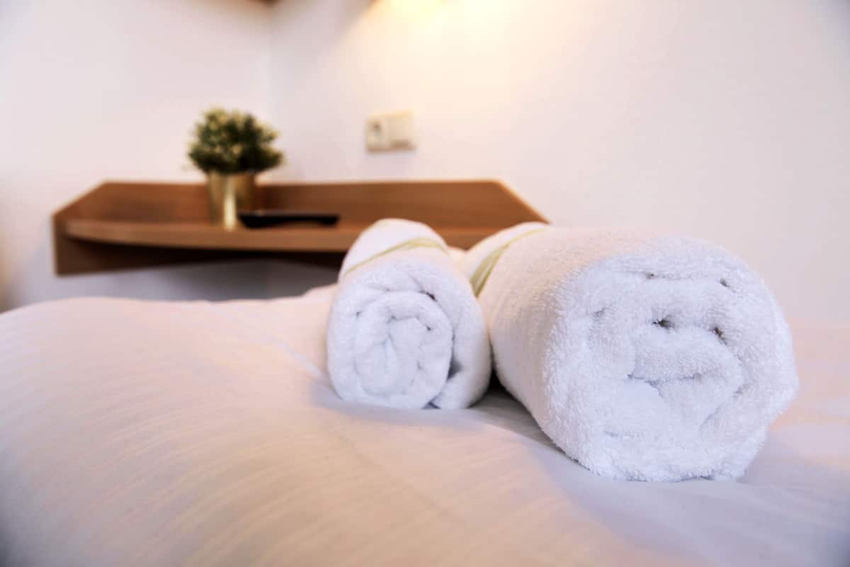 A neatly made bed with two rolled white towels and a small potted plant on a wooden side table.