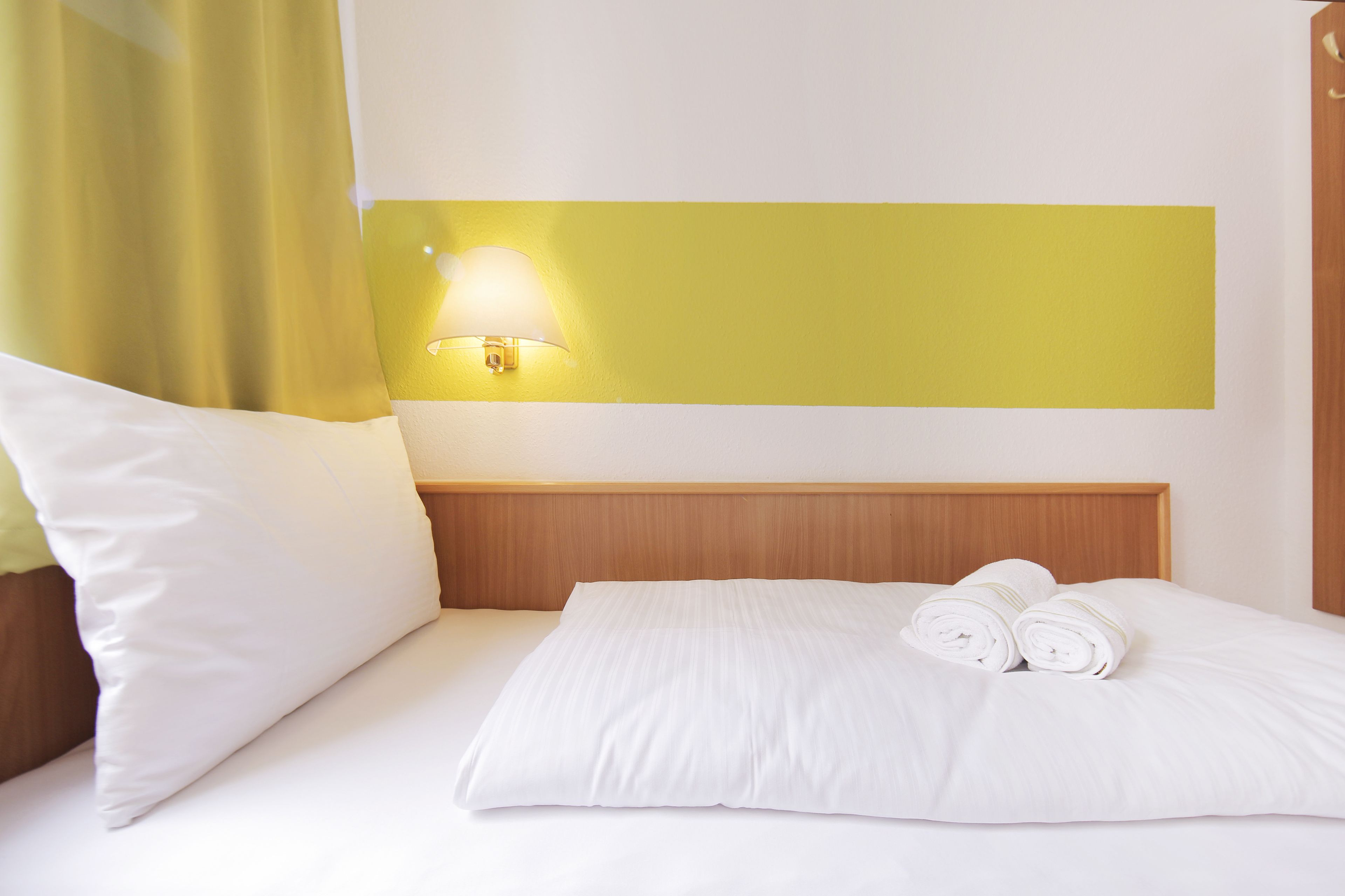Ein Hotelzimmer mit einem ordentlich bezogenen Bett, einer Wandlampe und einem Holzkopfteil.