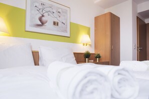 Quarto de hotel com uma cama, mesa de cabeceira com abajur, quadro na parede e guarda-roupa de madeira.