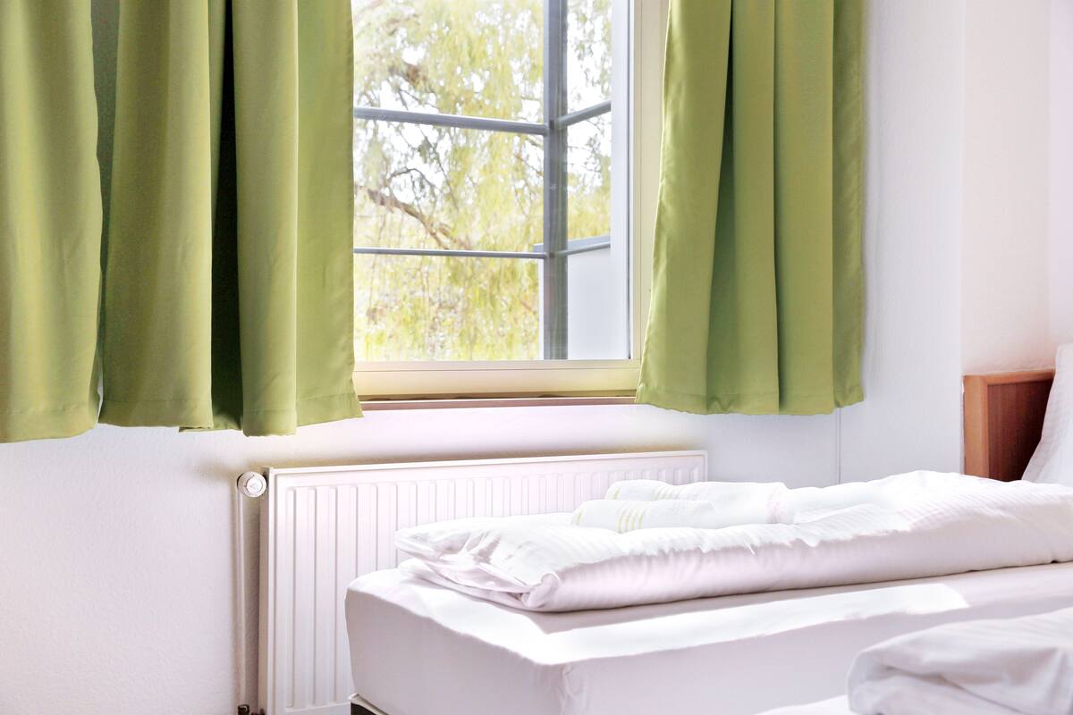 A bedroom with a window, white bedding, and a radiator.