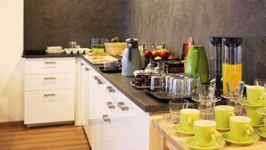 Un bufé de desayuno con diversos alimentos, una cafetera y un frutero.