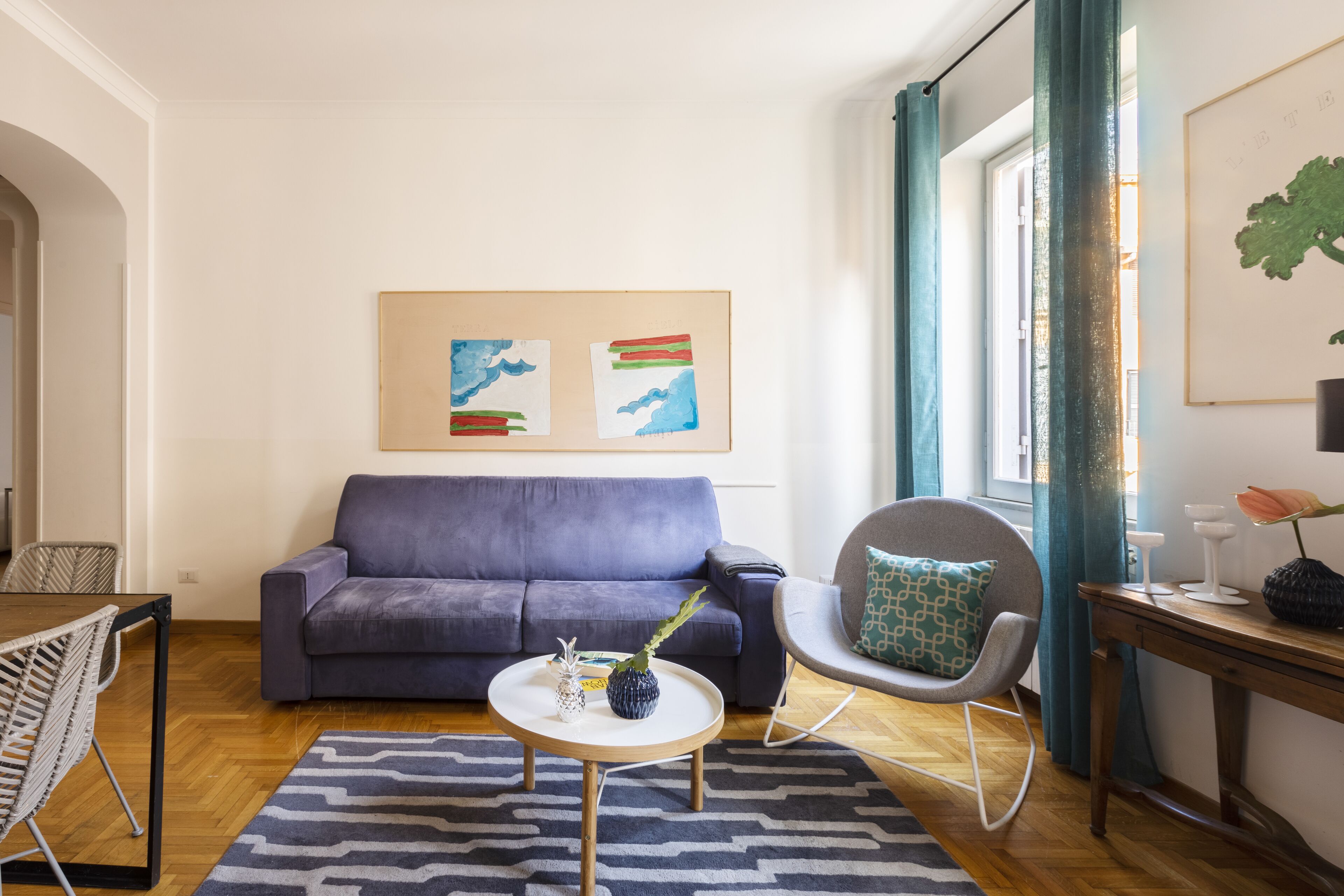 Ein Wohnzimmer mit einem blauen Sofa, einem runden Couchtisch, einem gemusterten Teppich und Bildern an der Wand.