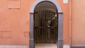A closed metal gate with a decorative archway, a number plaque, and a utility box on a building facade. - ROMAC - Condotti I (Rome)