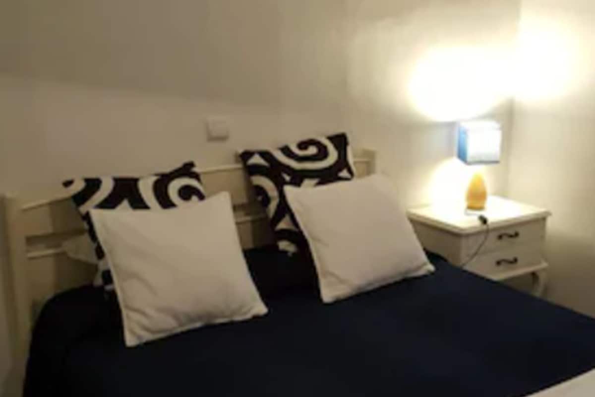 A double bed with white and navy bedding, a bedside lamp, and a wall-mounted painting.