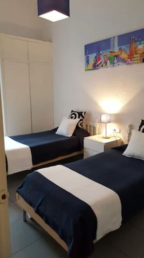 A room with two beds, a nightstand with a lamp, a painting on the wall, and a wardrobe. - Hostal Parisien (Barcelona)