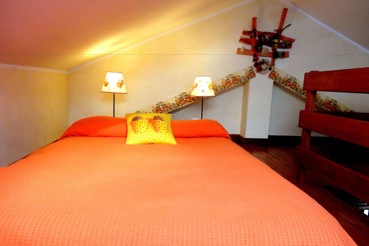 A bedroom with a large bed, two bedside lamps, a wooden bench, and a decorative wall piece.