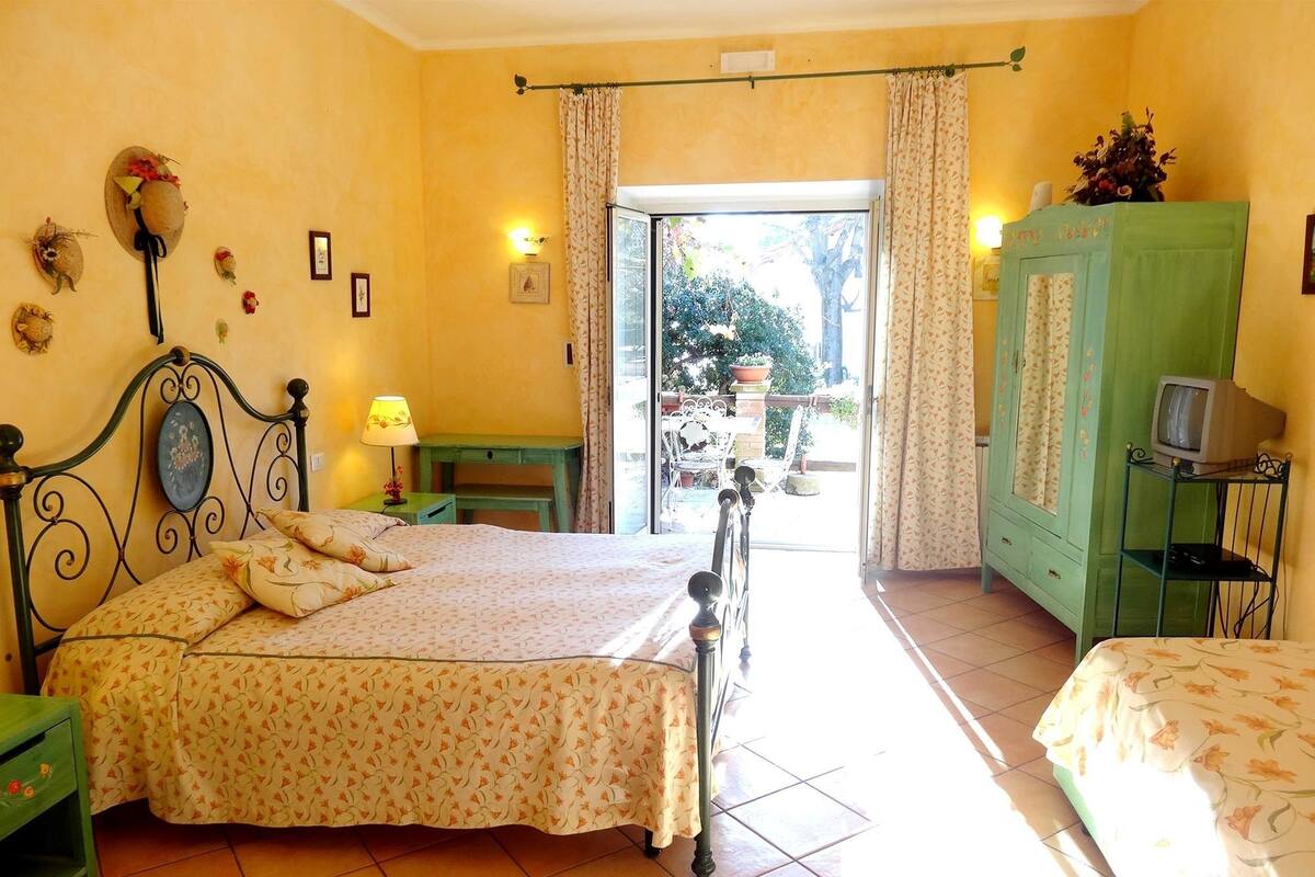 A bedroom with a bed, a green nightstand, a green dresser, a television on a stand, and a window with curtains.
