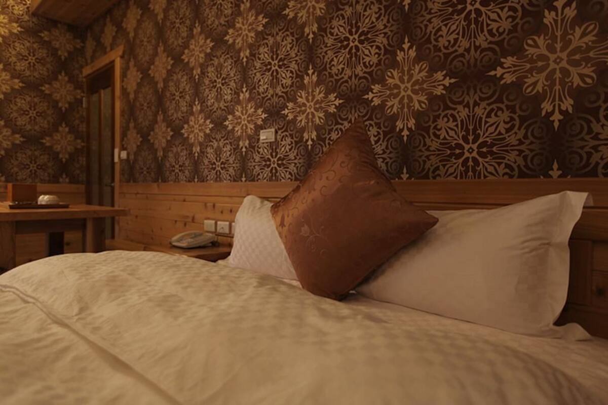 A bedroom with a patterned wallpaper, a wooden headboard, and a bedside table with a lamp.