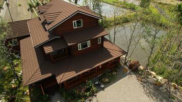 A two-story wooden house with a sloped roof, a front porch, and a small garden area with potted plants and a gravel driveway.