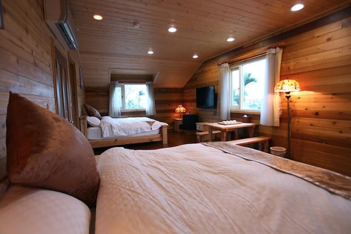A cozy cabin-style room with wooden walls, a bed, a desk, and a TV.