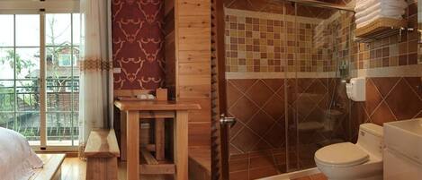 A wooden cabin with a bedroom, a small wooden table, a bench, a shower with a glass door, and a toilet.
