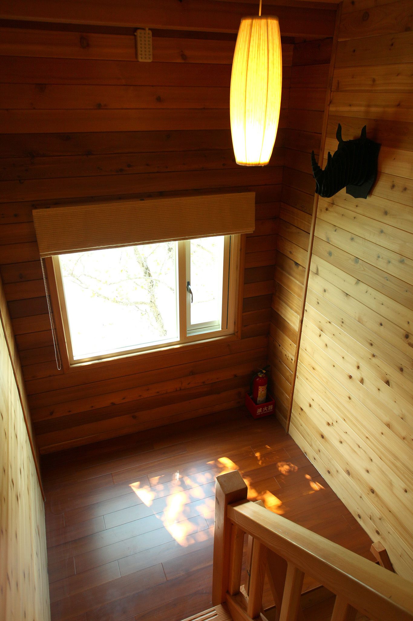 Interior de una cabaña de madera con techo inclinado, una ventana con vistas a árboles, un banco de madera y un adorno en la pared.