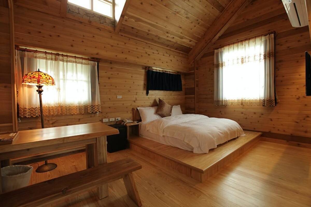 A wooden cabin bedroom with a bed, a nightstand, a lamp, and a window with curtains.