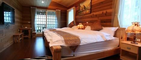 A wooden cabin room with a bed, a nightstand, a lamp, and a window with curtains.