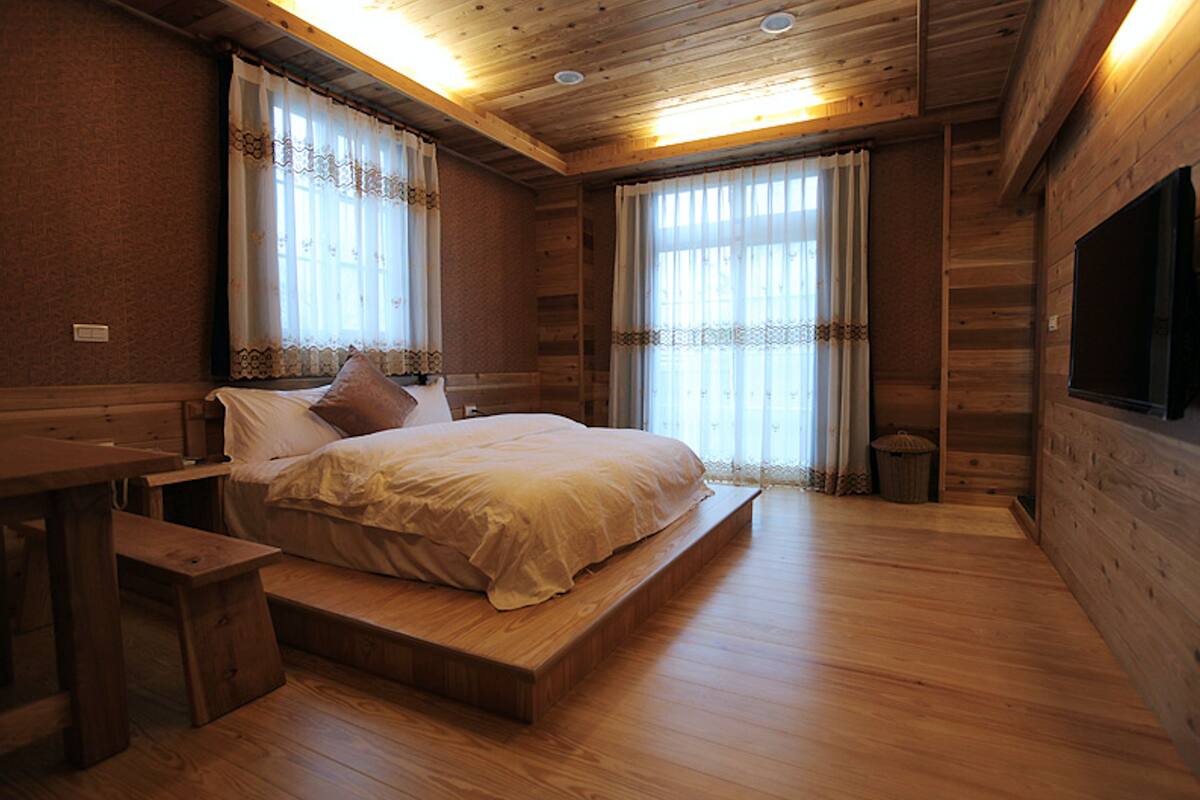 A wooden cabin-style bedroom with a large bed, a bench, and a TV mounted on the wall.