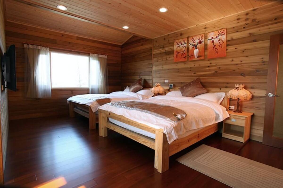 A wooden cabin bedroom with two beds, a window with curtains, and a wall-mounted artwork.