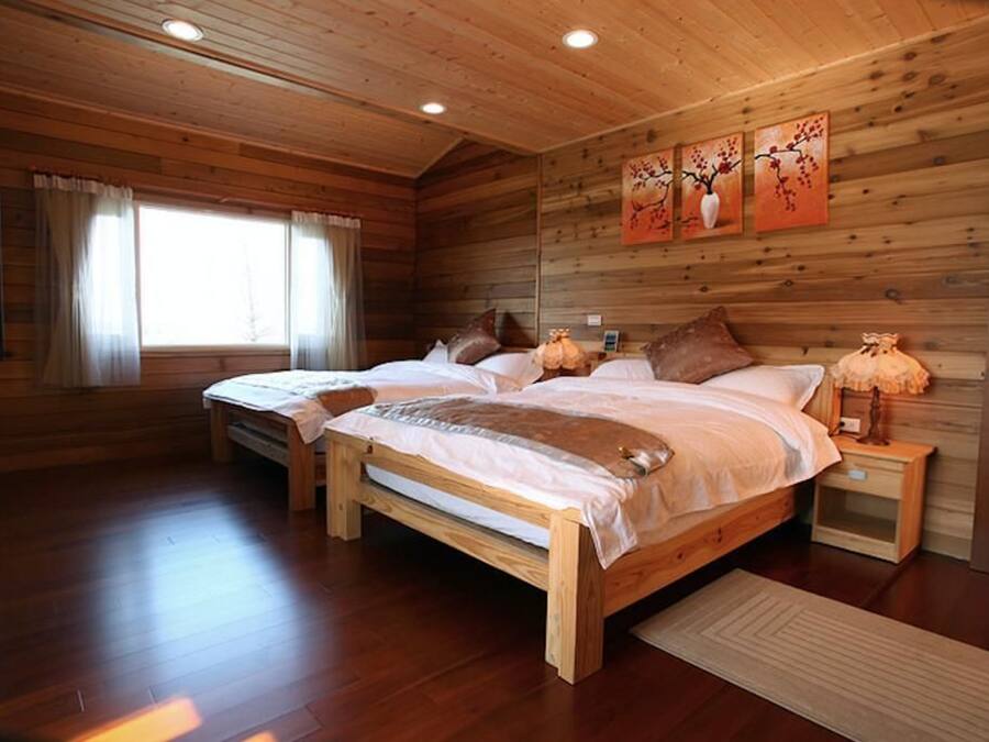 A wooden cabin bedroom with two beds, a window with curtains, and a wall-mounted artwork.