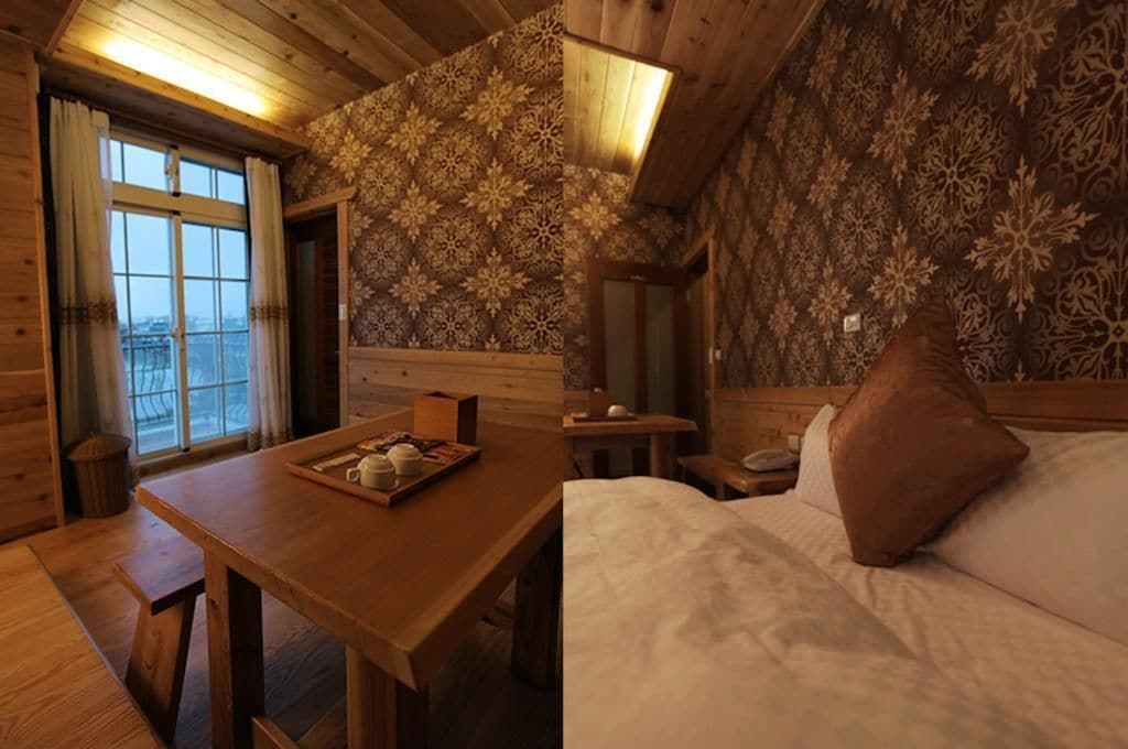 A cozy room with a wooden table, a bed with a pillow, a desk, and a patterned wall.