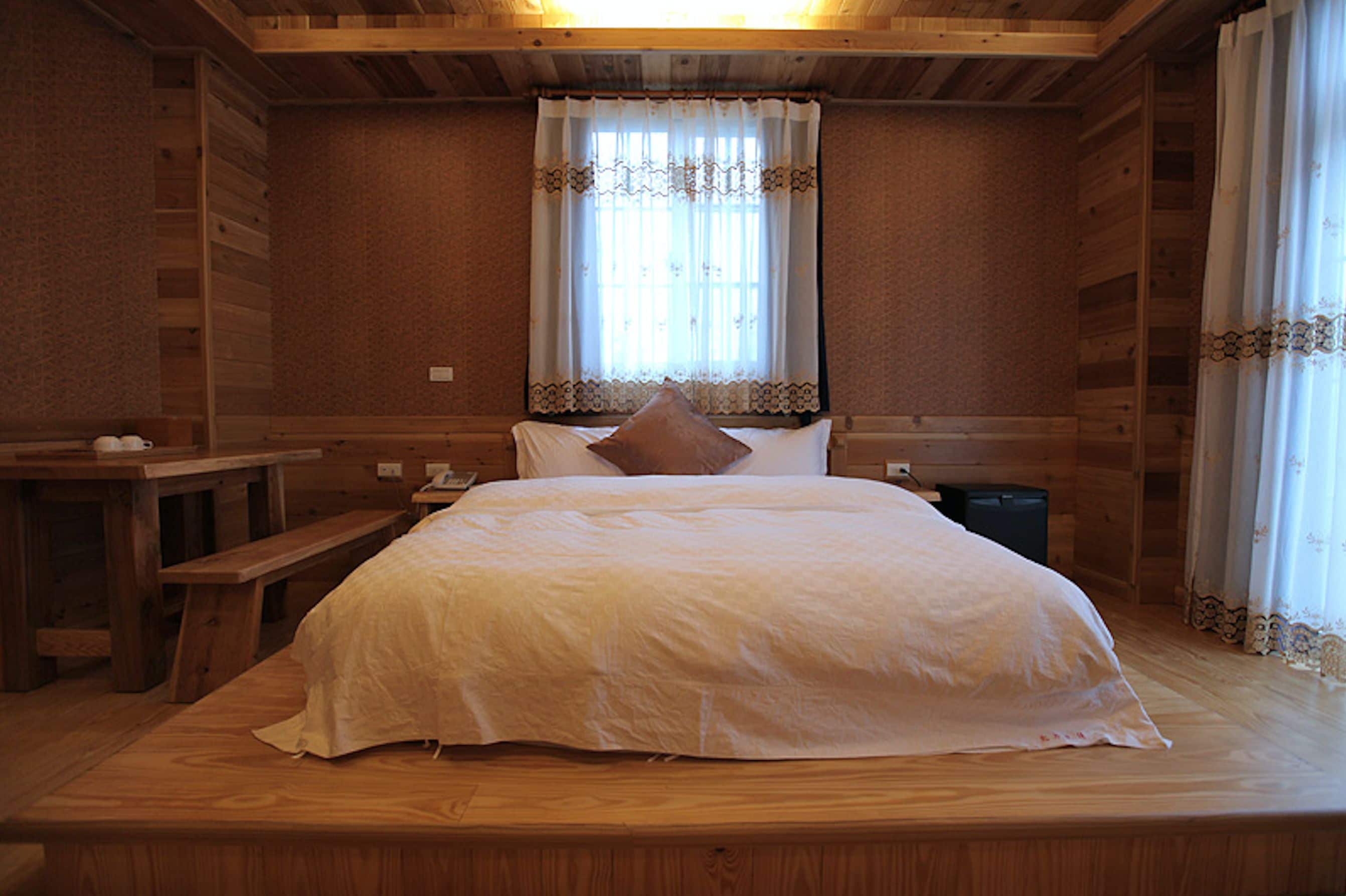 Un dormitorio de cabaña de madera con una cama, un banco y una ventana con cortinas.