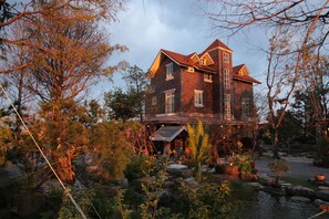 A large brick house with a steeply pitched roof, surrounded by a garden with rocks, plants, and a small pond. - North Zart Homestay (Dongshan)
